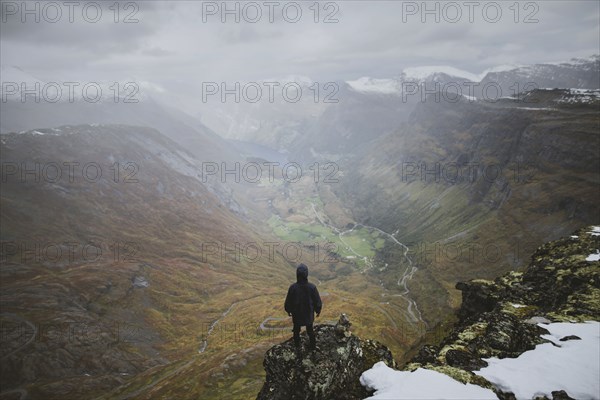 Man standing on Dalsnibba mountain overlooking valley in Geiranger, Norway