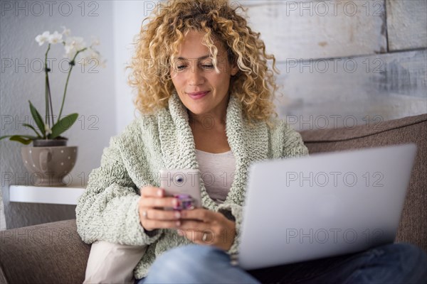 Smiling woman using smart phone and laptop on sofa