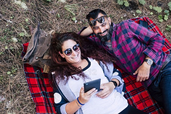 Smiling couple lying on blanket using tablet