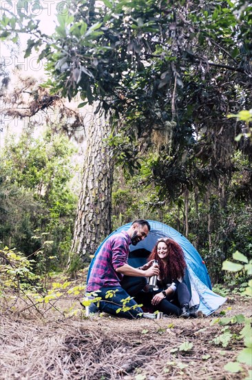 Smiling couple holding flask by tent