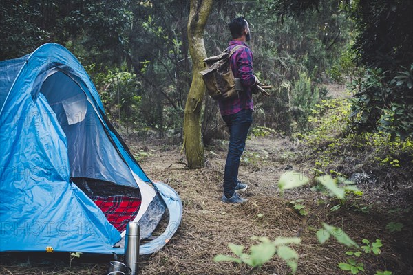 Man holding sticks by tent in forest