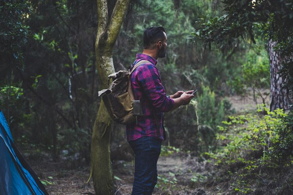 Man wearing backpack using smart phone in forest