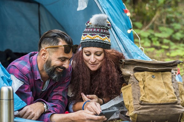 Smiling couple lying in tent using tablet