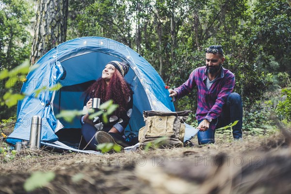 Smiling woman holding cup by man adjusting tent