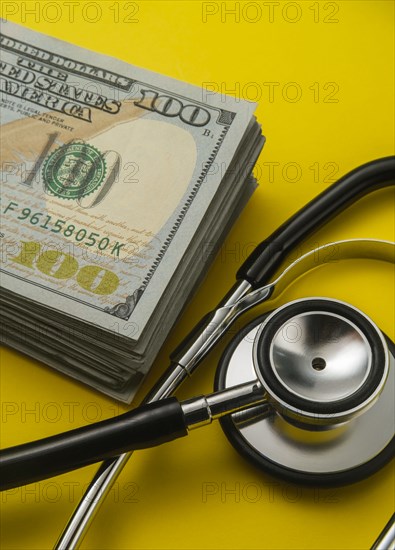 Stack of 100 dollar bills and stethoscope on yellow background