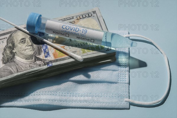 Covid-19 test vial and swab on stack of 100 dollar bills and medical mask