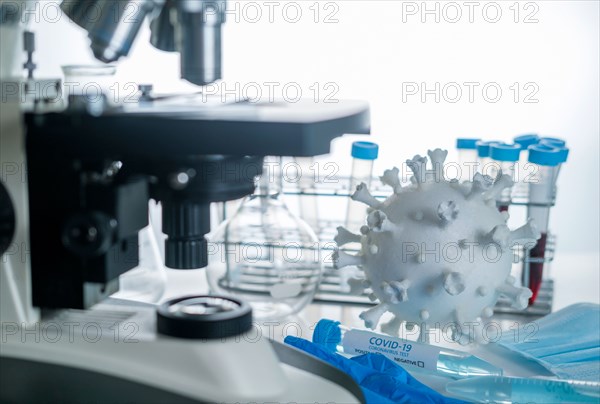 Microscope in laboratory with model of coronavirus and test vials