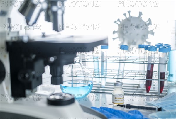 Microscope in laboratory with model of coronavirus,  vials, and vaccine