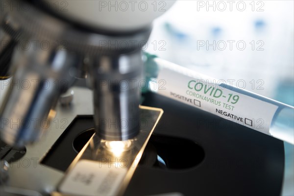 Laboratory microscope with a slide and vial of coronavirus test