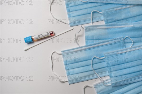 Blue medical masks and test tube with blood sample on white background