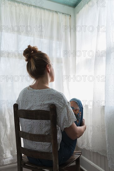 Woman sitting in front of curtained windows