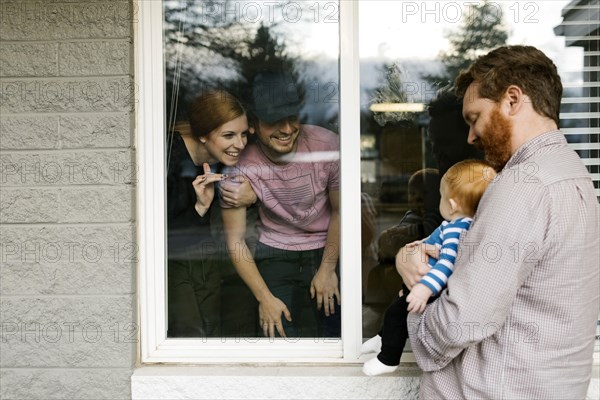 USA, Florida, Fort Myers Beach, Man with baby son (2-5 months) visiting family through window