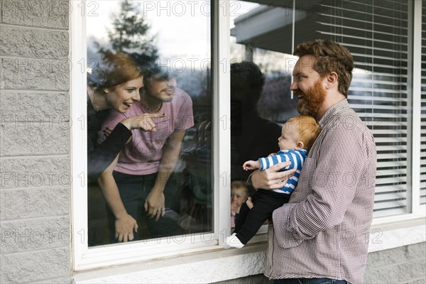 USA, Florida, Fort Myers Beach, Man with baby son (2-5 months) visiting family through window