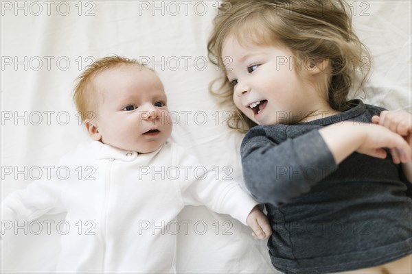 Siblings (2-5 months, 2-3) lying on bed