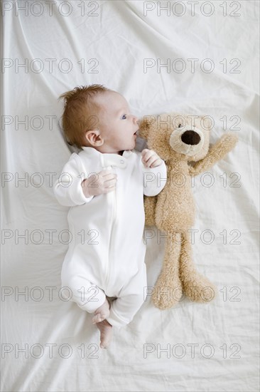 Baby boy (2-5 months) lying on bed with teddy bear