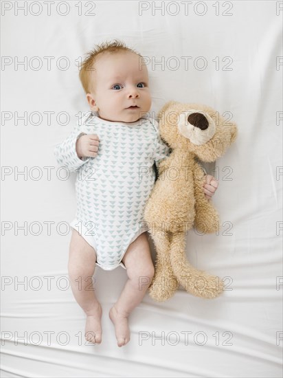 Baby boy (2-5 months) lying on bed with teddy bear