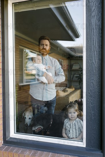 Father with children (2-5 months, 2-3) looking through window