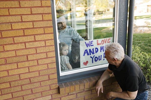 Grandfather visiting family with granddaughter (2-3) through window