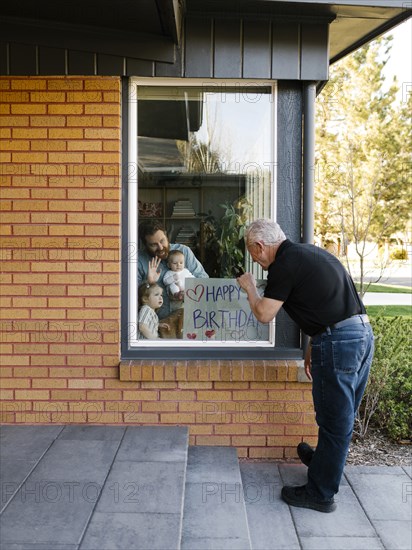 Grandfather visiting family with grandchildren (2-3 months, 2-3) through window