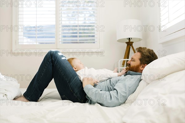 Father lying on bed with baby boy (2-3 months)