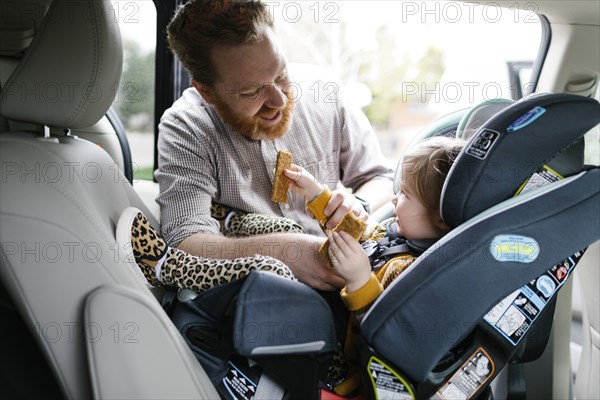Father buckling daughter (2-3) in car seat