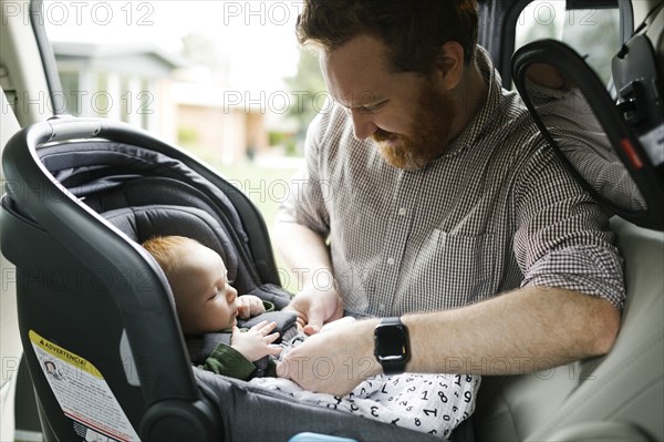 Father buckling baby boy (2-3 months) in car seat