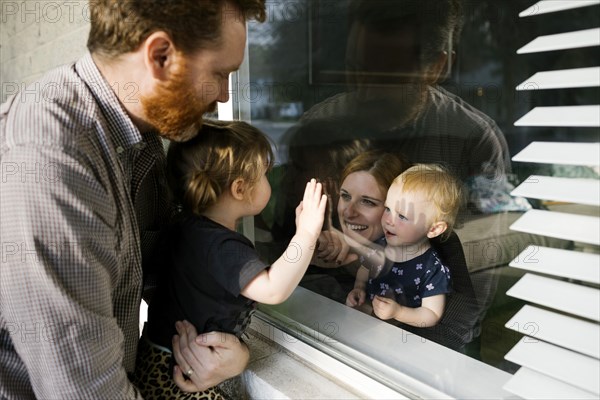 Family with daughters (2-3) visiting through window