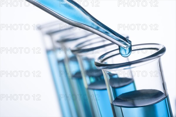 Close-up of blue drop on pipette and row of test tubes