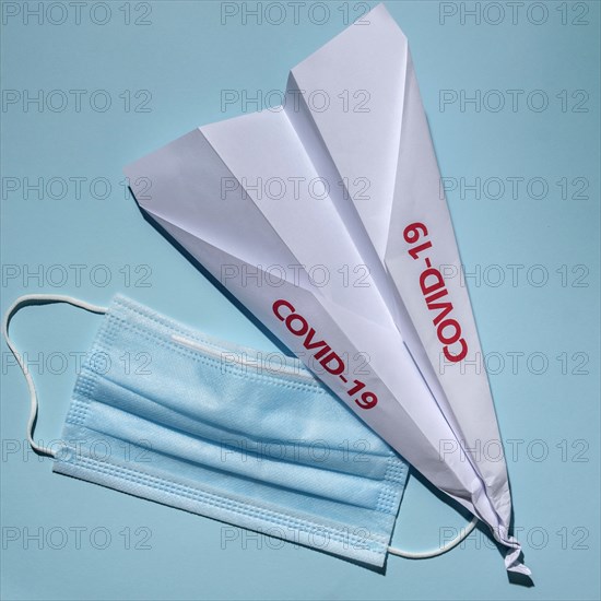 Studio shot of paper plane with Covid-19 sign and surgical mask