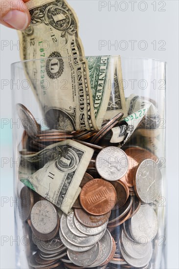 Close-up of fingers pulling one dollar bill from jar with American cents and banknotes