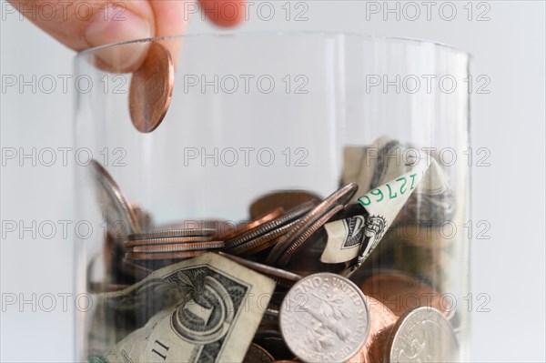 Close-up of fingers putting American cent into jar with coins and banknotes