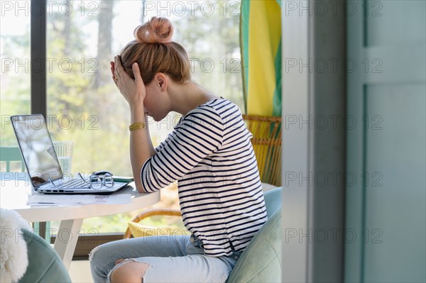 Woman sitting in front of laptop with head in hands