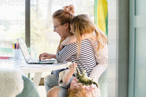 Children (4-5, 6-7) climbing on their mother while she works from home