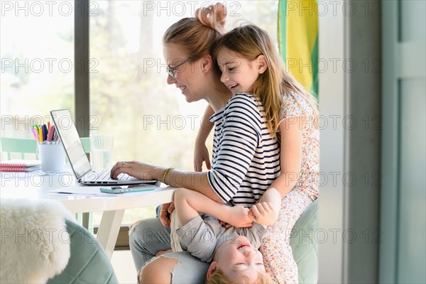 Children (4-5, 6-7) climbing on their mother while she works from home