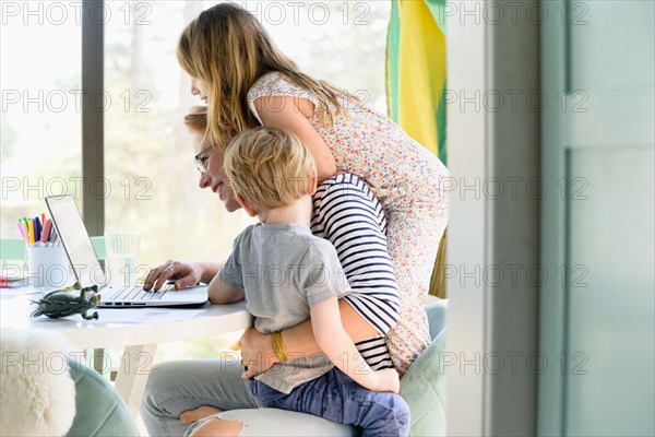 Children (4-5, 6-7) climbing on their mother while she works from home