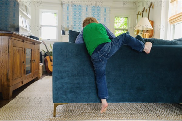 Rear view of boy (4-5) climbing over back of couch