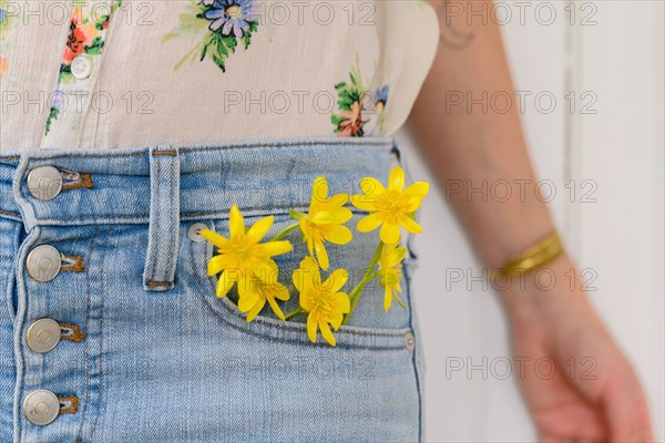 Close-up of woman with yellow flowers in jeans pocket