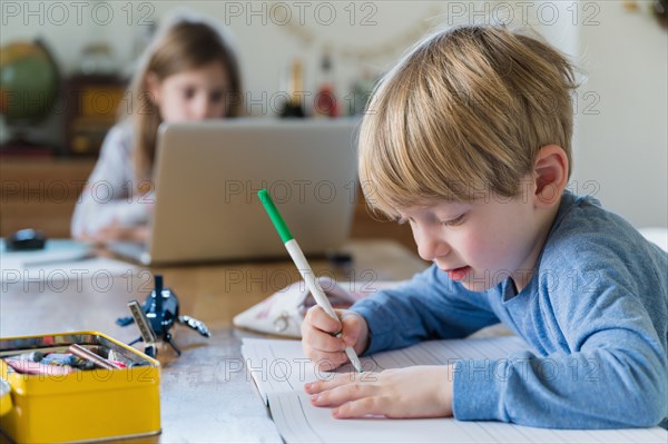 Boy (4-5) and girl (6-7) doing homework at table