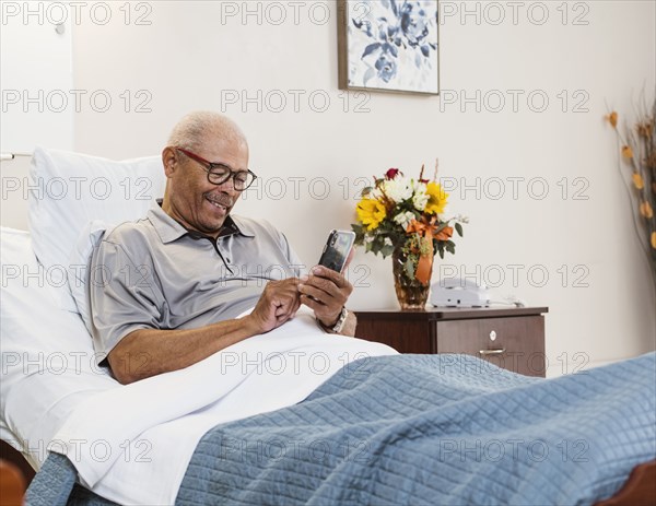 Senior man lying in bed and using smart phone