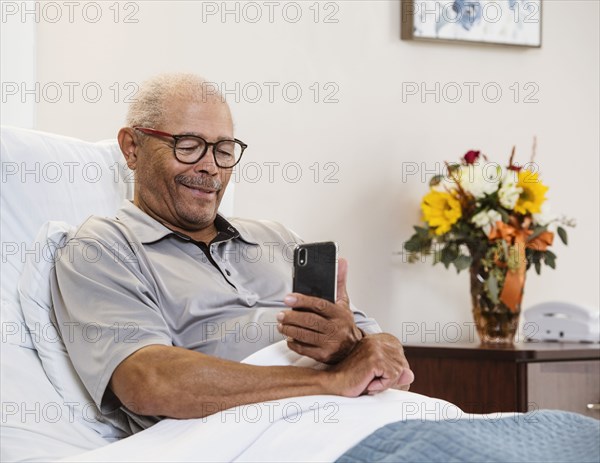 Senior man lying in bed and using smart phone