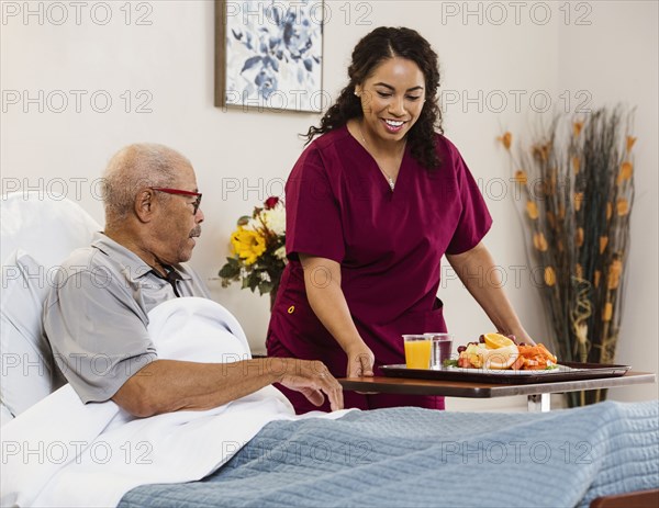 Nurse bringing healthy meal to senior man in bed