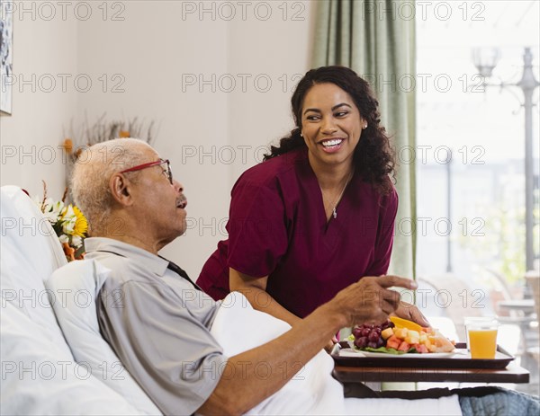 Nurse bringing healthy meal to senior man in bed