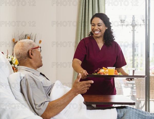 Nurse bringing healthy meal to senior man in bed