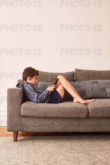 Boy (8-9) using tablet on sofa