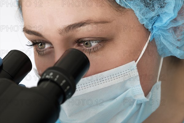 Laboratory technician in face mask looking through microscope