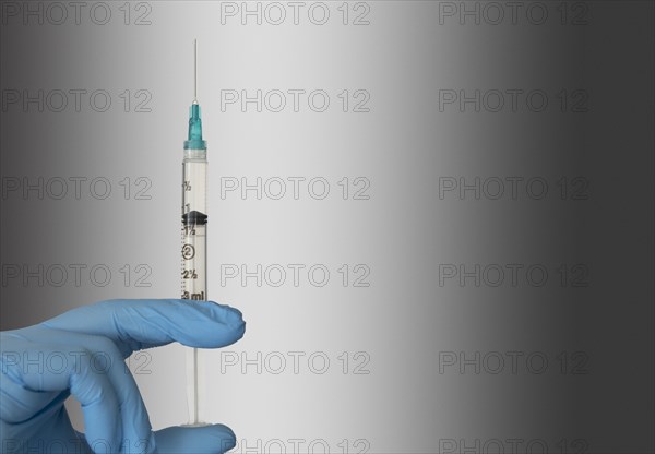 Close-up of hand in blue surgical glove holding syringe