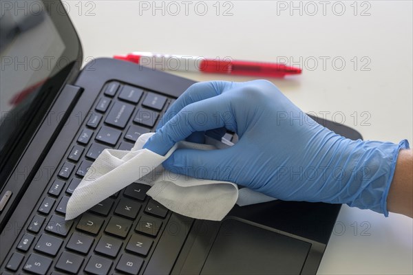Person wearing blue surgical glove cleaning keyboard of laptop
