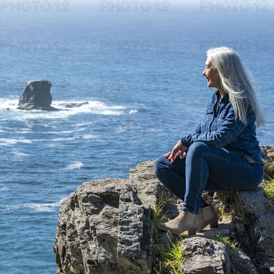 USA, California, Big Sur, Woman sitting at the edge of cliff looking at view