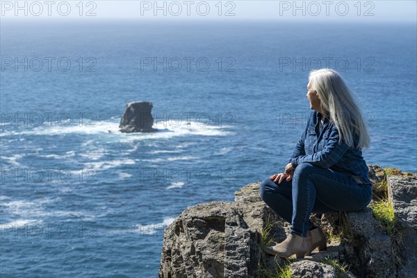 USA, California, Big Sur, Woman sitting at the edge of cliff looking at view