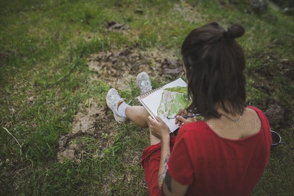 Switzerland, Obergoms, Young woman painting with watercolor in Swiss Alps